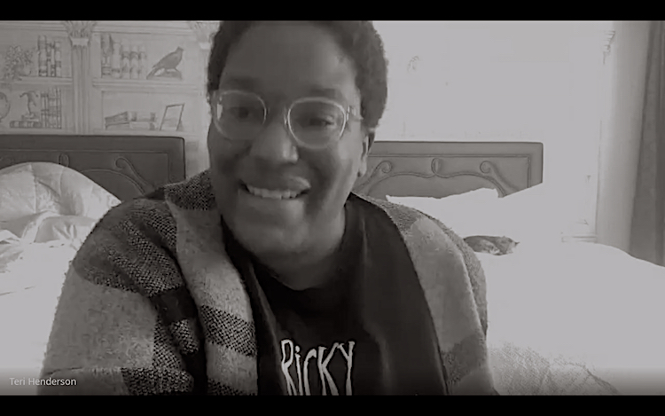 Black and white image of Teri Henderson, a young black woman with short hair and glasses in a modest hotel room with two beds in the background. The beds have rectangular wooden headboards. On the beds are white linens, and a cat is curled up on the bed on the right.